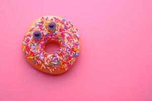 A colorful donut adorned with a variety of sprinkles set against a pink background photo