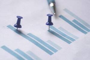 Detailed Business Chart Displayed with Colorful Push Pins and a Pen Resting on Paper Surface photo