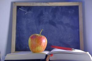 An image features an apple placed on books with a blackboard background in an educational setting photo