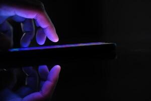 A closeup of a hand using a glowing smartphone in dark space, showcasing modern tech photo