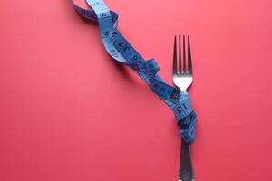 A fork and a measuring tape on a vibrant red background a concept of dieting and nutrition photo