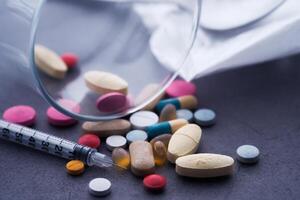 A collection of assorted medications and a syringe resting on a dark surface background photo