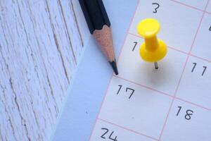 A CloseUp Image of a Calendar Featuring a Pencil and a Bright Yellow Push Pin on a Wooden Table photo