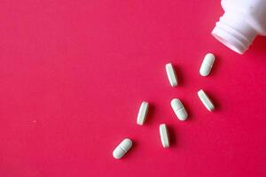 A multitude of white pills are spilling out from a bottle set against a vivid red background photo