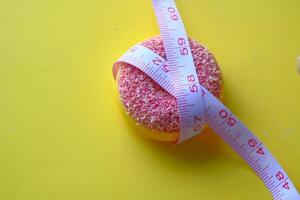 Measuring a bright pink donut using a tape measure against a vibrant yellow background photo