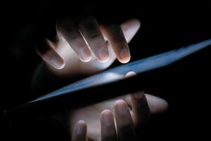 A persons hands interact with a tablet screen in low light, creating an engaging atmosphere photo