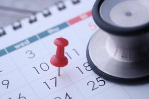 A stethoscope and a red thumbtack placed on a calendar signify health appointments and schedules photo