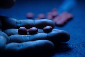 A hand is holding red pills illuminated by blue light, suggesting healthrelated themes photo