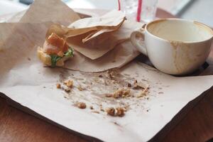 There is a leftover coffee and a snack carelessly left on the dining table waiting photo