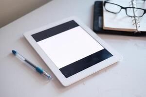 A modern workspace with a stylish tablet, sleek notebook, and glasses on a desk photo