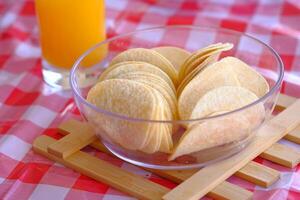 Enjoy tasty potato chips in a glass bowl with a refreshing orange drink for a delightful snack photo