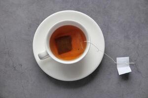 A Tea Bag is Steeping in a Cup of Warm Tea While Positioned on a Rough Stone Surface photo