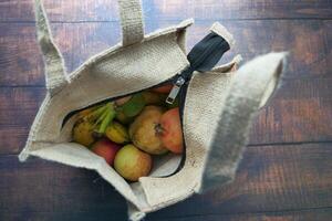 An overhead view of a tote bag filled with fresh fruits on a wooden table surface photo