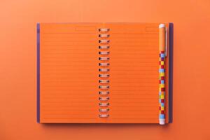 A Vibrant Orange Notebook is Open with a Colorful Pen Laying on a Light Background Surface photo