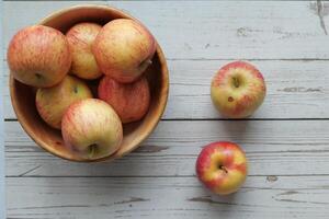 A collection of Fresh Apples arranged beautifully in a Wooden Bowl on a Rustic Table photo