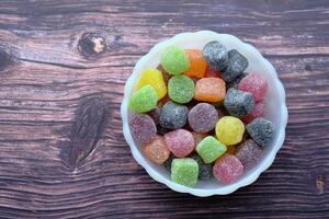 A Vibrant and Colorful Assorted Candy Displayed in a White Bowl on a Rustic Wooden Background photo