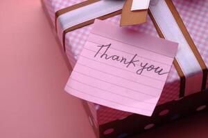 A Beautifully Decorated Gift Wrapped Elegantly with a Heartfelt Thank You Note on a Pink Background photo