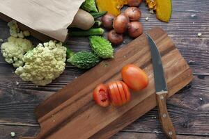 A variety of Fresh Vegetables, including Chopped Tomatoes, displayed on a Wooden Cutting Board photo