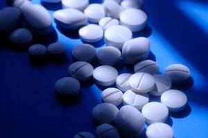 Scattered white pills on a vibrant blue background with dramatic lighting effects photo