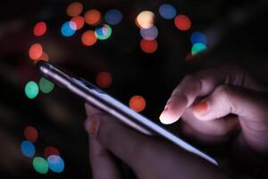 A person attentively using a smartphone surrounded by a vibrant and colorful bokeh background photo