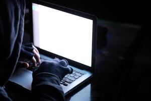 A hacker is working diligently on a laptop in a dark environment, creating a sense of mystery photo