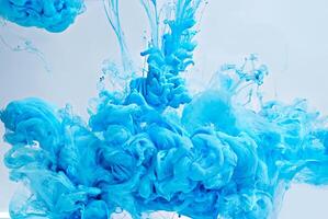 Abstract closeup of vibrant blue ink swirling and dispersing in water, creating cloud-like shapes in a fluid dynamic motion. photo