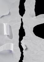 Close-up of torn white paper with a jagged tear down the center, revealing a black background. Suitable for abstract or background use. photo