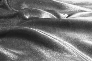 Close-up of shimmering metallic fabric texture with soft folds and smooth surface in monochromatic tones. photo