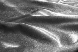 Close-up of shimmering metallic fabric texture with soft folds and smooth surface in monochromatic tones. photo