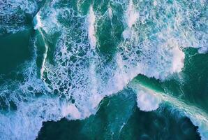 A stunning aerial view of ocean waves crashing into the shoreline, creating frothy white surf. photo