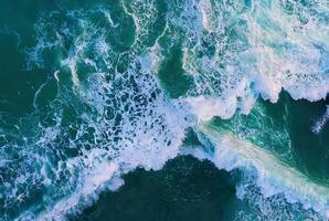 A stunning aerial view of ocean waves crashing into the shoreline, creating frothy white surf. photo