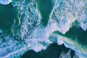 A stunning aerial view of ocean waves crashing into the shoreline, creating frothy white surf. photo