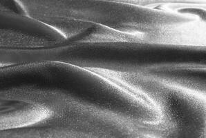 Close-up of shimmering metallic fabric texture with soft folds and smooth surface in monochromatic tones. photo