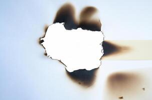 A burnt hole in white paper with irregular scorched edges and slight smoke marks, ideal for use in design projects or as a texture element. photo