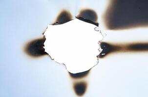 A burnt hole in white paper with irregular scorched edges and slight smoke marks, ideal for use in design projects or as a texture element. photo