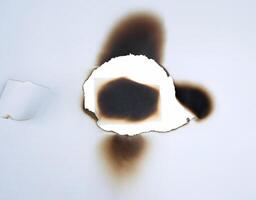 A burnt hole in white paper with singed edges, offering a unique texture for design elements or backgrounds. photo