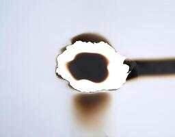 A burnt hole in white paper with singed edges, offering a unique texture for design elements or backgrounds. photo