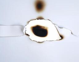 A burnt hole in white paper with singed edges, offering a unique texture for design elements or backgrounds. photo