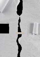Close-up of torn white paper with a jagged tear down the center, revealing a black background. Suitable for abstract or background use. photo