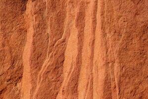 Close-up of red sandstone rock texture featuring natural wavy patterns and rough surface. photo