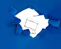 Torn blue paper with a jagged hole revealing a white background, perfect for creative and design concepts. photo