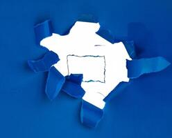 Torn blue paper with a jagged hole revealing a white background, perfect for creative and design concepts. photo