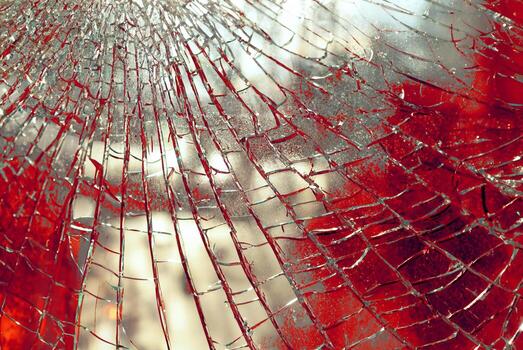 Close-up of shattered glass with red background and sunlight creating sharp reflections. photo
