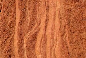 Close-up of red sandstone rock texture featuring natural wavy patterns and rough surface. photo