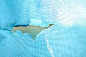 Close-up of a torn blue fabric with a rip in the center, showing visible texture and wear, ideal for concepts of damage or imperfection. photo