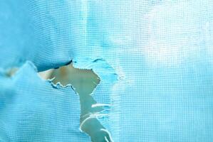 Close-up of a torn blue fabric with a rip in the center, showing visible texture and wear, ideal for concepts of damage or imperfection. photo