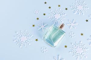 An unbranded perfume bottle on a blue background among decorative snowflakes and golden stars. top view. A copy space. blank bottle mockup. template photo
