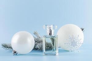 A beautiful bottle of perfume against the background of a snow-covered spruce branch and white Christmas balls. Front view. Product presentation photo