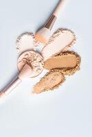Several loose powder samples in different tones on a white vertical background, two makeup brushes and a block of compact powder. top view. layout photo