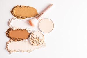 Beautiful loose powder samples in different tones, two blocks of compact powder and a makeup brush on a light background. top view. A copy space. photo